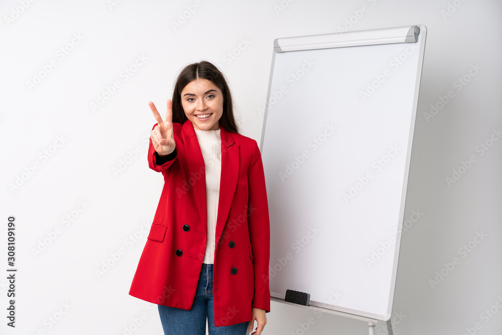 Young woman giving a presentation on white board smiling and showing victory sign Young woman giving a presentation on white board smiling and showing victory sign