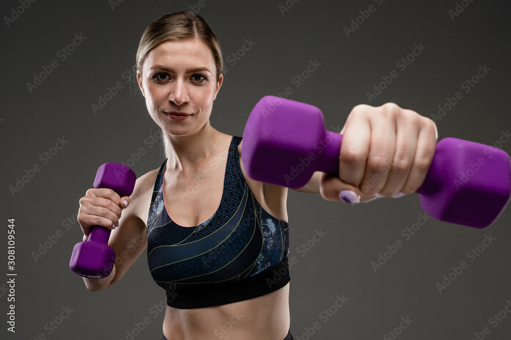 Sport caucasian girl with slim figure do exercises with purple dumddells isolated on black background Sport caucasian girl with slim figure do exercises with purple dumddells isolated on black background