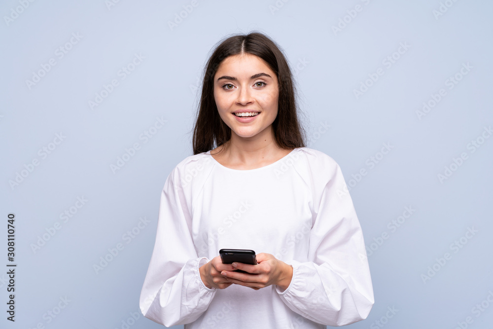 Young woman over isolated blue background sending a message or email with the mobile Young woman over isolated blue background sending a message or email with the mobile