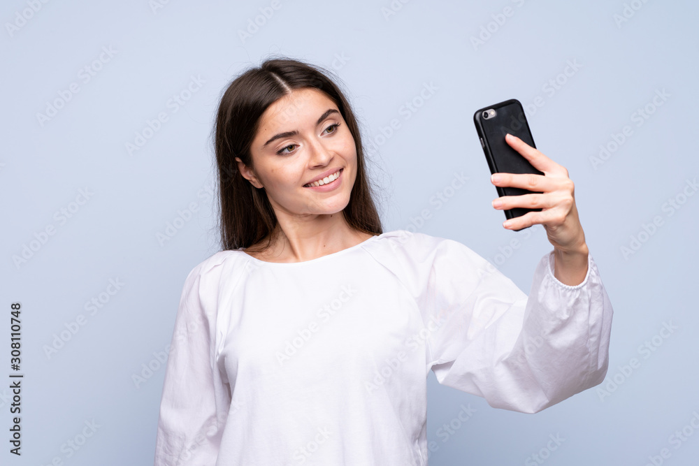 Young woman over isolated blue background taking a selfie with the mobile Young woman over isolated blue background taking a selfie with the mobile