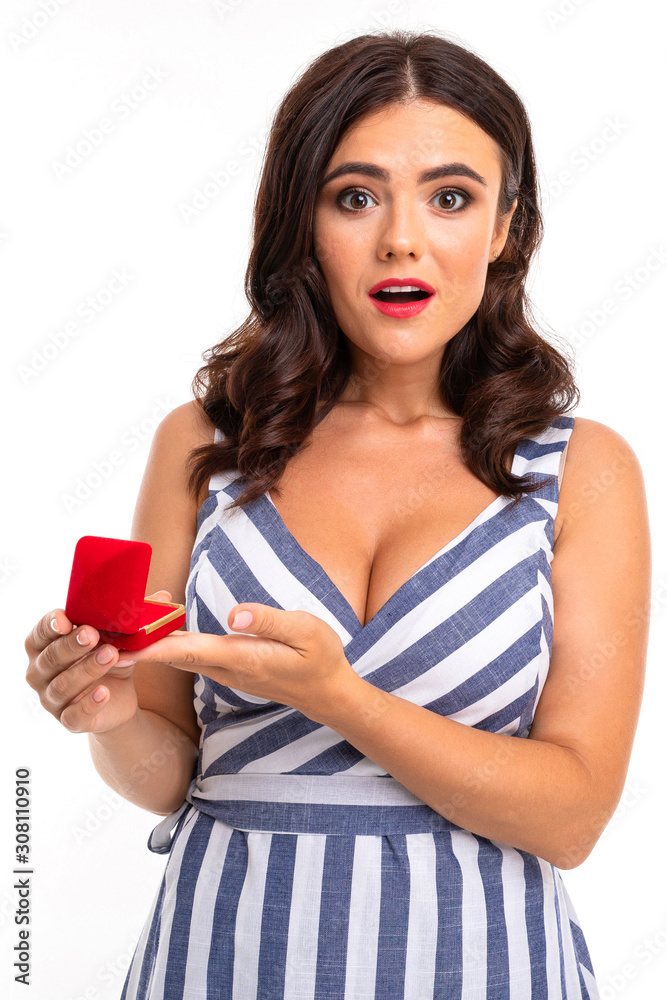 surprised young girl with brown hair in a dress with a neckline holds a box with an engagement ring on a white studio background surprised young girl with brown hair in a dress with a neckline holds a box with an engagement ring on a white studio background