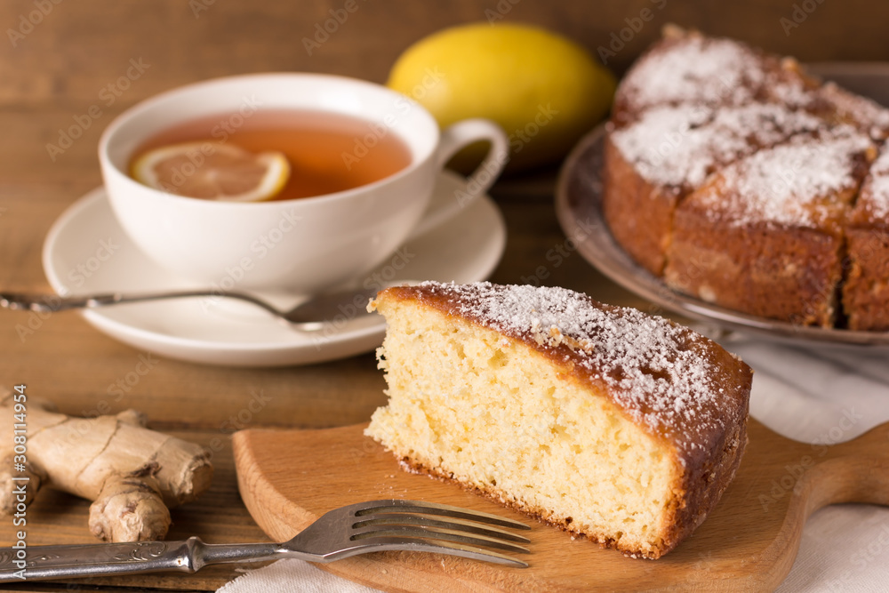 piece of homemade lemon pie, lemon, ginger and a cup of tea on a wooden background