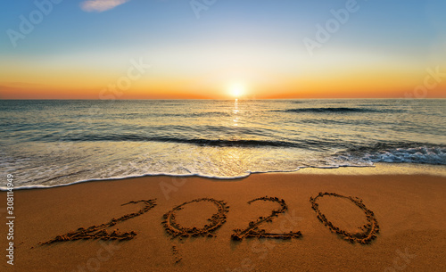 Welcome 2020 written on the sand beach, with beautiful sunrise background.