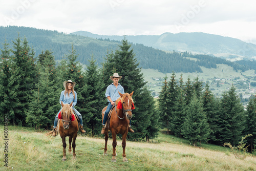 Couple riding horses in countryside tour - Happy people having fun on summer day outdoor - Vacation, excursion, healthy lifestyle, sport, love between people and animals concept photo