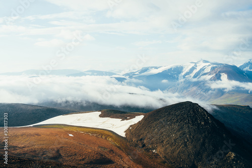 Atmospheric alpine landscape with giant low cloud above rocky mountain with glacier. Big thick cloud above highland valley. Wonderful scenery on high altitude. Flying over mountains above clouds.