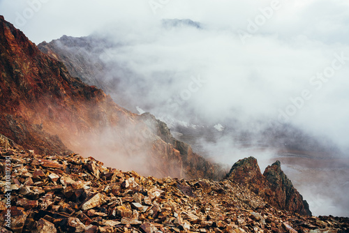 Beautiful pointy cliff on high rocky mountain edge above precipice with thick low clouds. Atmospheric minimalist alpine landscape. Pointed craggy stone near abyss in clouds. Wonderful highland scenery