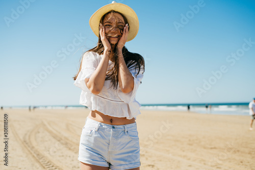 Photos girl laughs and joyfully put her hands to her cheeks, stands on a sandy beach