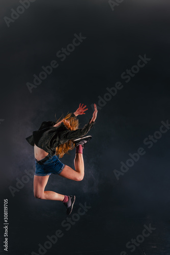 Fototapeta Naklejka Na Ścianę i Meble -  Elastic female dancer jumps high in the air while there is a lot of smoke in the background.