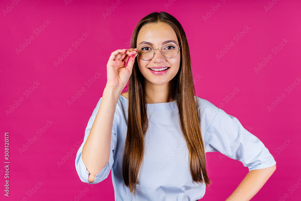 the girl in glasses for sight holds them by the handle and smiles cute while looking at the screen. background pink the girl in glasses for sight holds them by the handle and smiles cute while looking at the screen. background pink