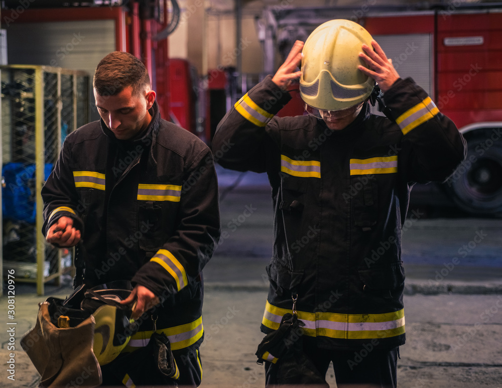 Portrait of two young firemen in uniform standing inside the fire station . Portrait of two young firemen in uniform standing inside the fire station .