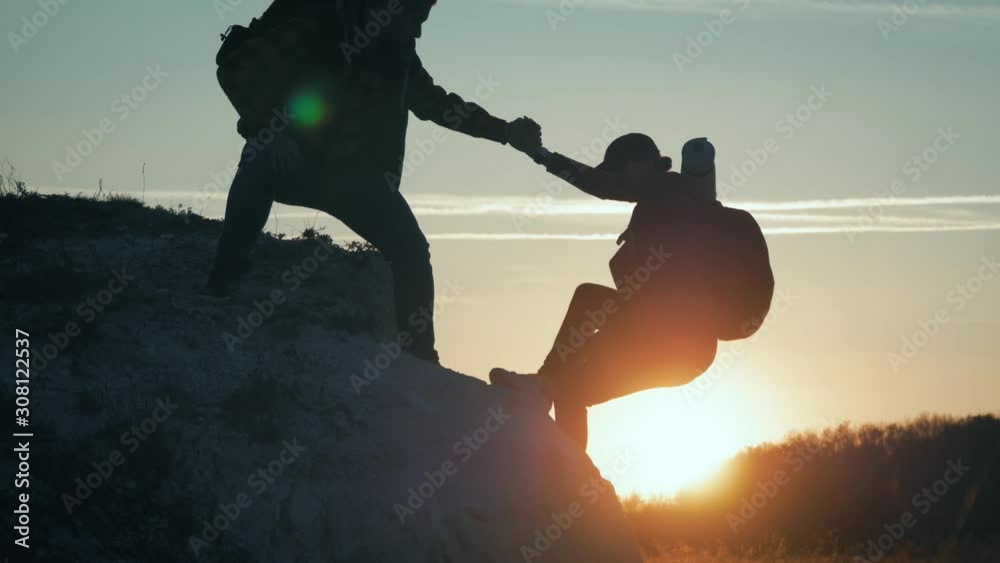 Couple hiking help each other silhouette in mountains. Teamwork couple hiking, help each other, trust assistance, sunset. Man giving hand a woman to help her to climb the mountain.