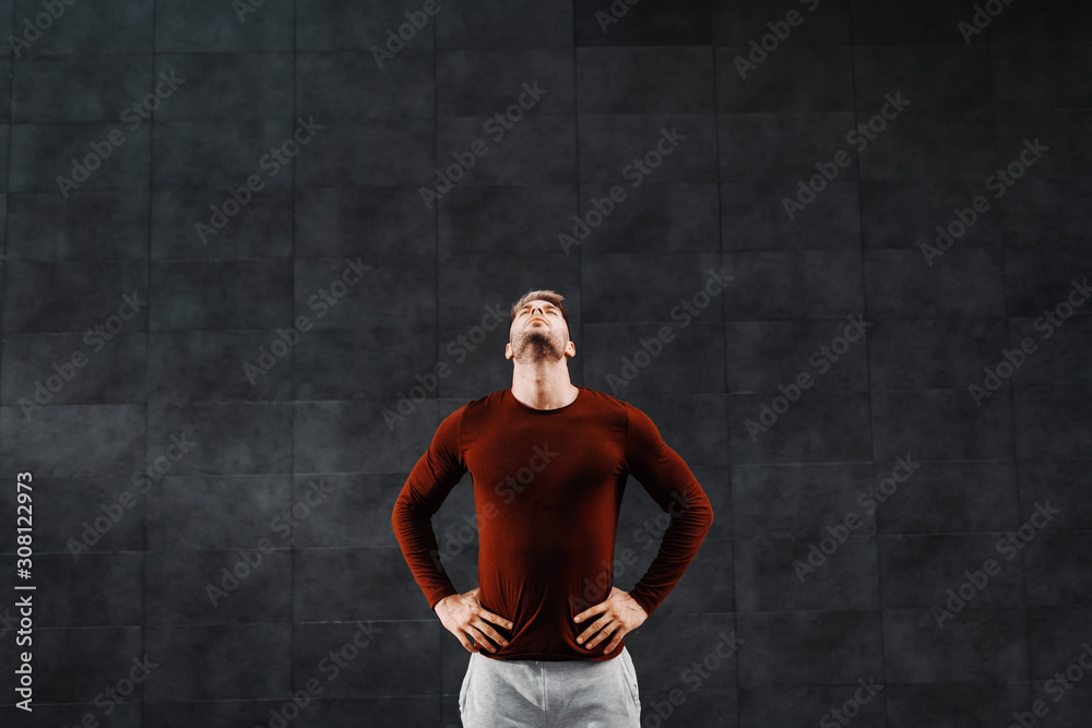 Obraz premium Attractive fit caucasian breaded sportsman in tracksuit holding hands on hips and doing warm up exercises for neck before running.