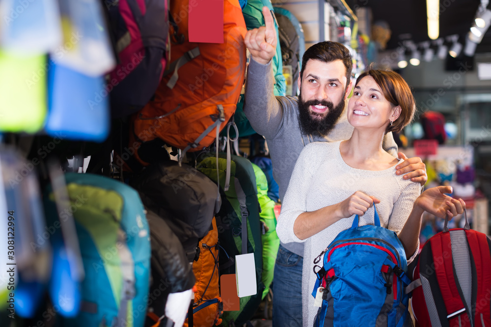 glad couple examining rucksacks in sports equipment store