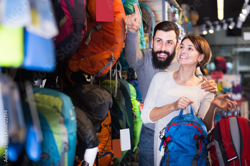 glad couple examining rucksacks in sports equipment store