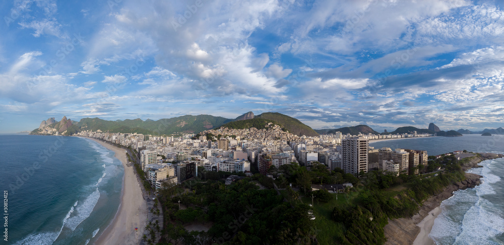 Aerial wide panorama of Rio de Janeiro seen from the Arpoador rock with Ipanema and Copacabana beach in the foreground and wider cityscape in the background against a cloudy sky