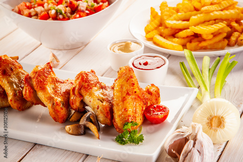 Barbecued chicken wings with french fries and vegetable salad on timber