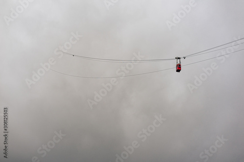 Photo of a cable way in the mountains. Red cableway cabine in the air diving into the clouds. Cableway to the top of Lomnicky stit, High Tatras, Slovakia.