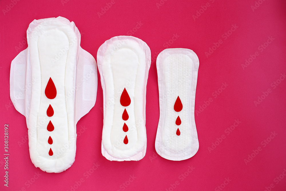 White woman cotton menstruation pads of different sizes with wings with red paper drops on pink background. White woman cotton menstruation pads of different sizes with wings with red paper drops on pink background.