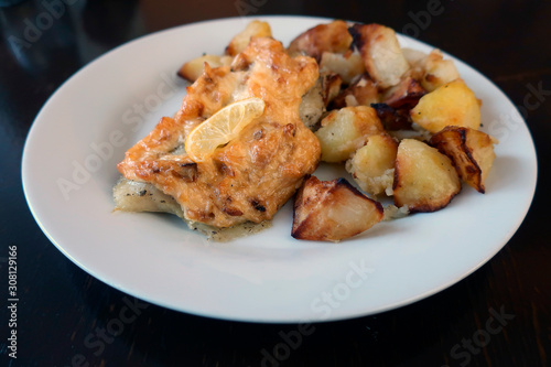 baked fish with potatoes and a slice of lemon in a restaurant on a white plate