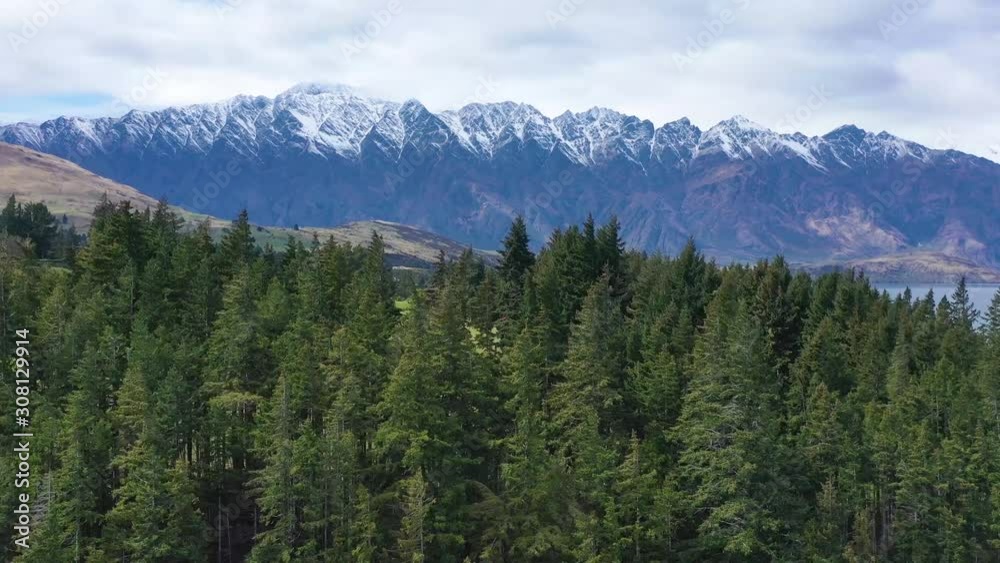 2019 - aerial shot over trees reveals Queenstown, New Zealand and Remarkables mountain range. 2019 - aerial shot over trees reveals Queenstown, New Zealand and Remarkables mountain range.