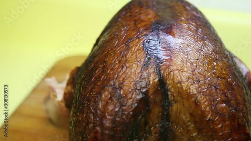 Panning up and across the rear end of a smoked Thanksgiving turkey. The texture of the crisp skin looks delicious and an electric carving knife cuts the meat of the bird into slices. Jiggles when cut.