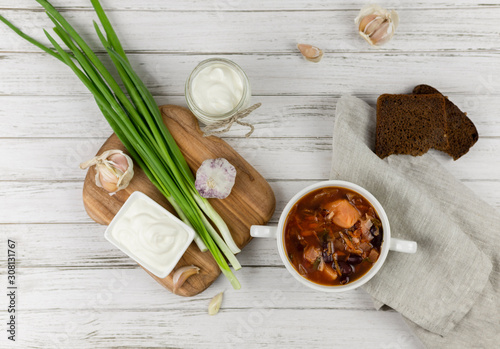 red borsch  a traditional national dish of Ukrainian cuisine. on the stock photo is served in a white plate with sour cream  green onions and garlic on a light wooden background using gray textile