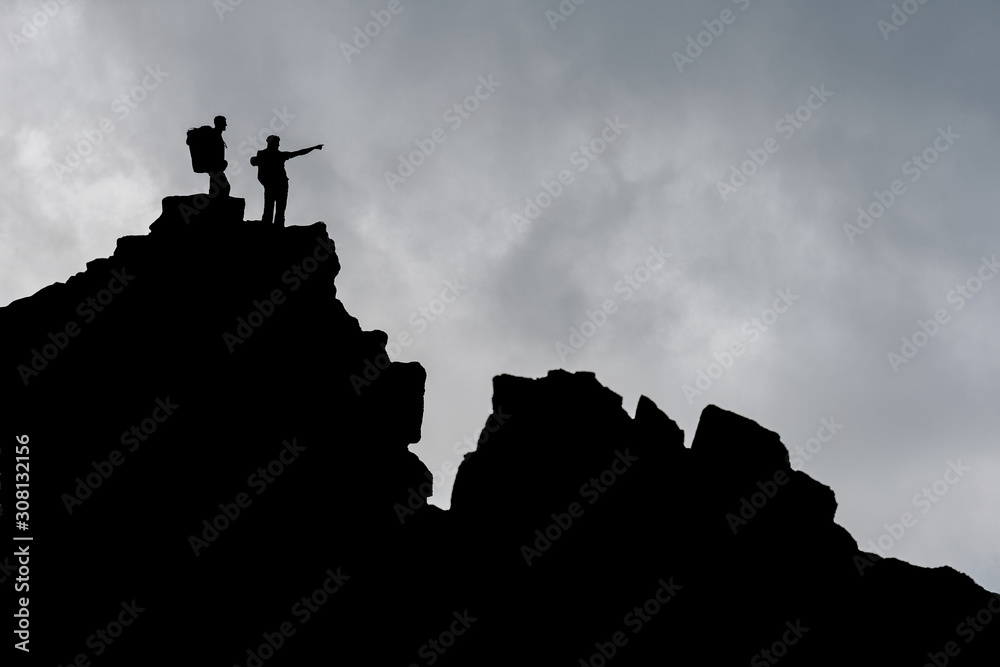 Two men standing on s rock and pointing to the distance. Mountain explorer collage. Double exposure of hikers with backpacks on a moutain view. Background or wallpaper image with landscape sunset.