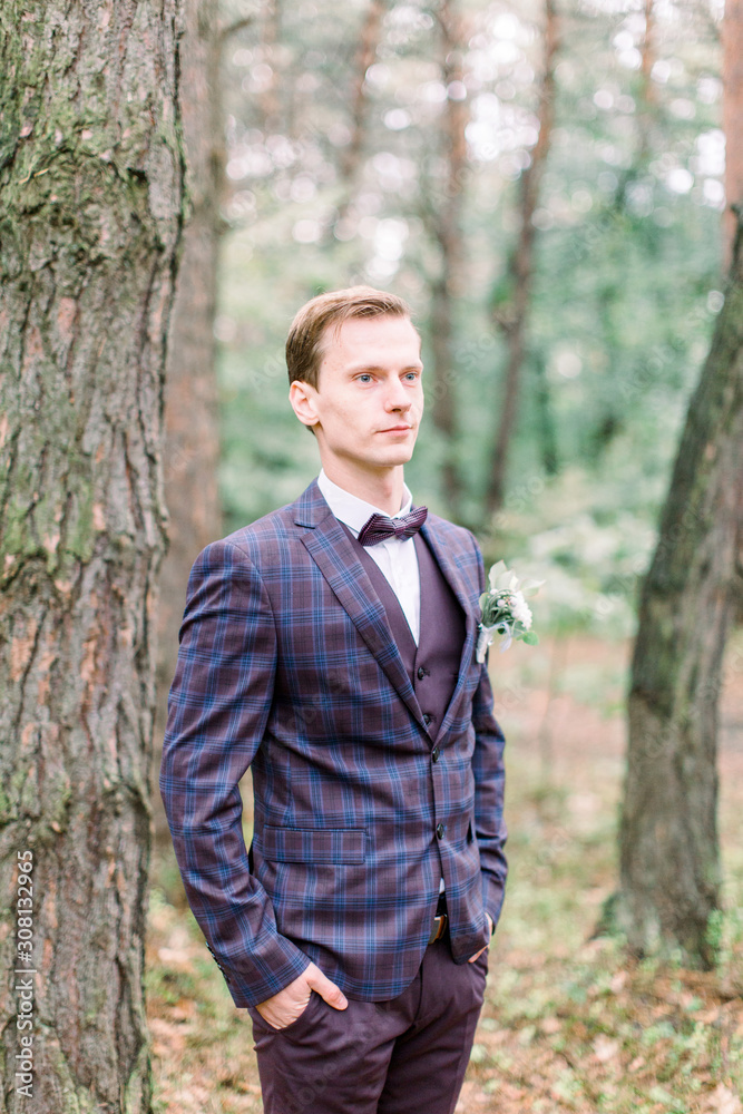Handsome elegant groom in checkered dark violet suit is standing in the forest. Stylish wedding grooms photo. Rustic portrait. Handsome elegant groom in checkered dark violet suit is standing in the forest. Stylish wedding grooms photo. Rustic portrait.
