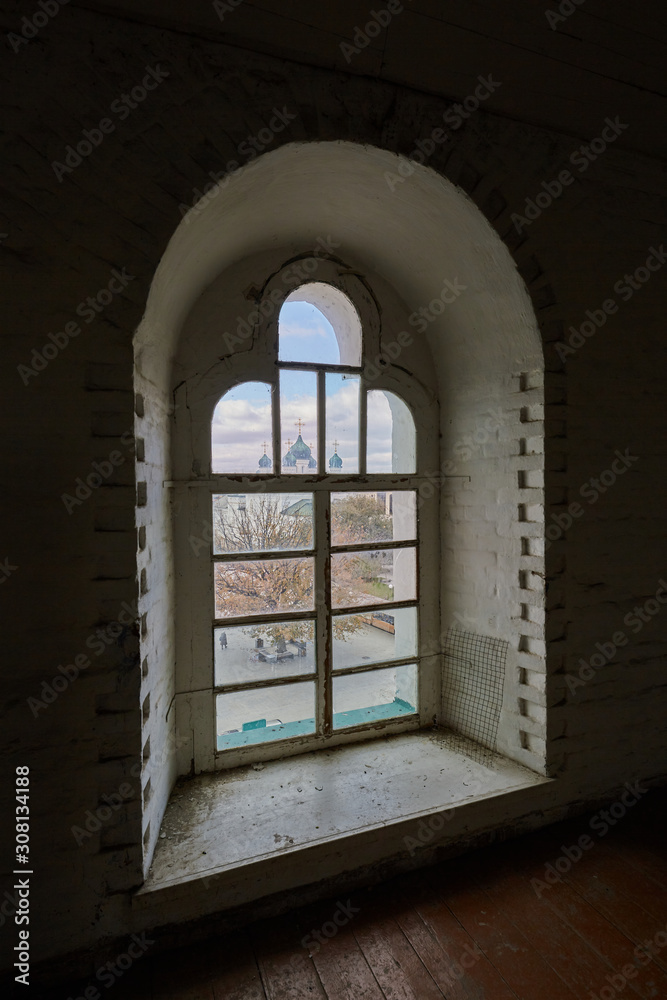Domes of the old church are visible through the arched window of the old tower