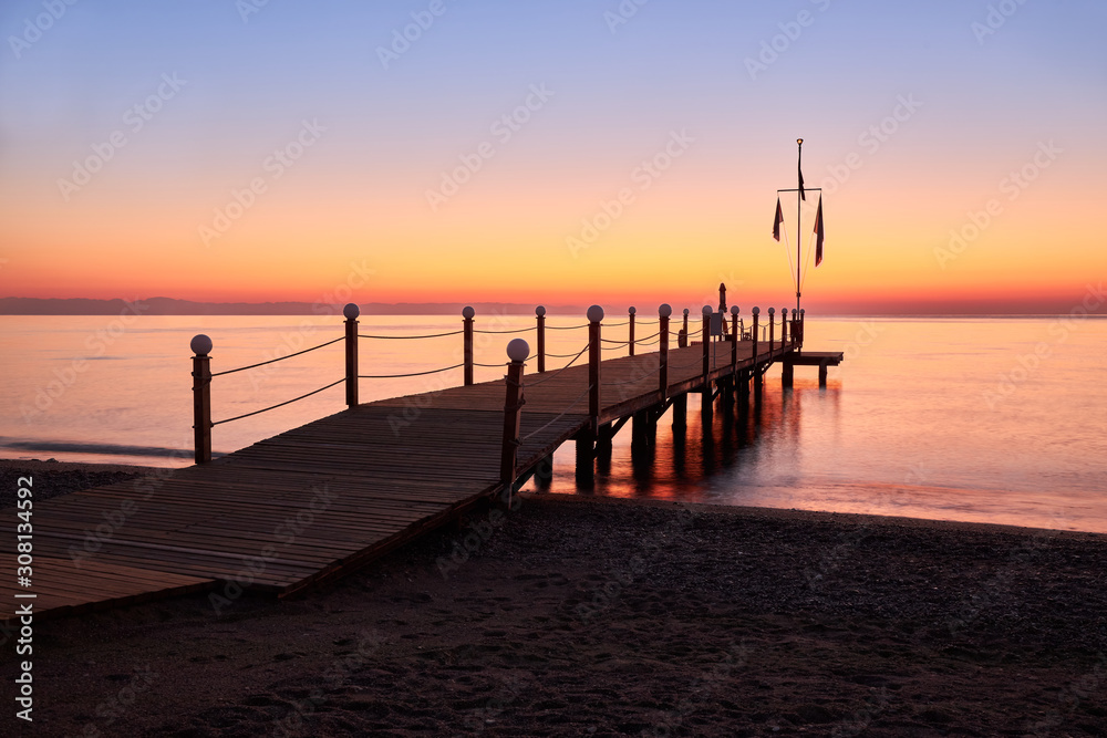 Calm warm sea and a large wooden pier with a swimming area at dawn