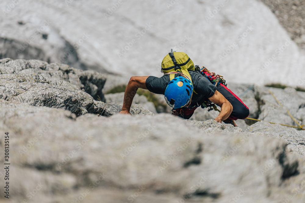 Obraz premium A climber or a mountaineer ascending a big rock face. Man, an alpinist, on extreme adventure sport climb in big rock wall. Climbing in High Tatras, Slovakia.