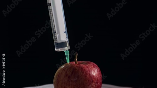 Syringe stuck in apple on plate isolated in black background photo