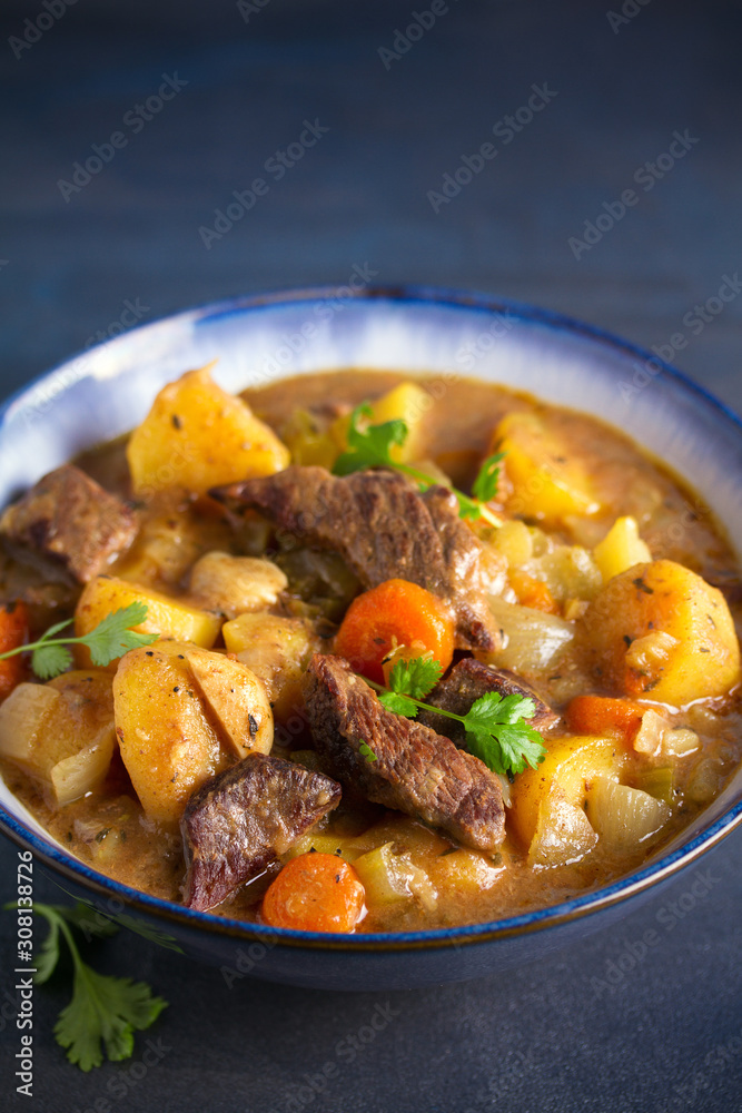 Beef meat stewed with potatoes, carrots and spices in bowl on dark gray background. vertical image Beef meat stewed with potatoes, carrots and spices in bowl on dark gray background. vertical image