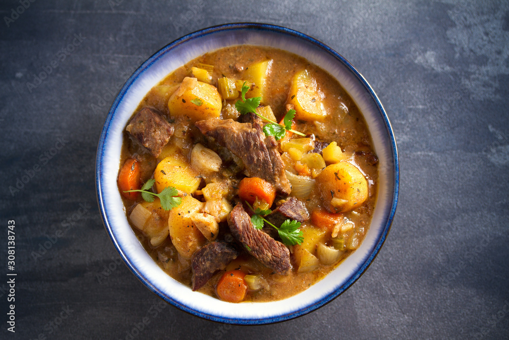 Beef meat stewed with potatoes, carrots and spices in bowl on dark gray background. Overhead horizontal image Beef meat stewed with potatoes, carrots and spices in bowl on dark gray background. Overhead horizontal image