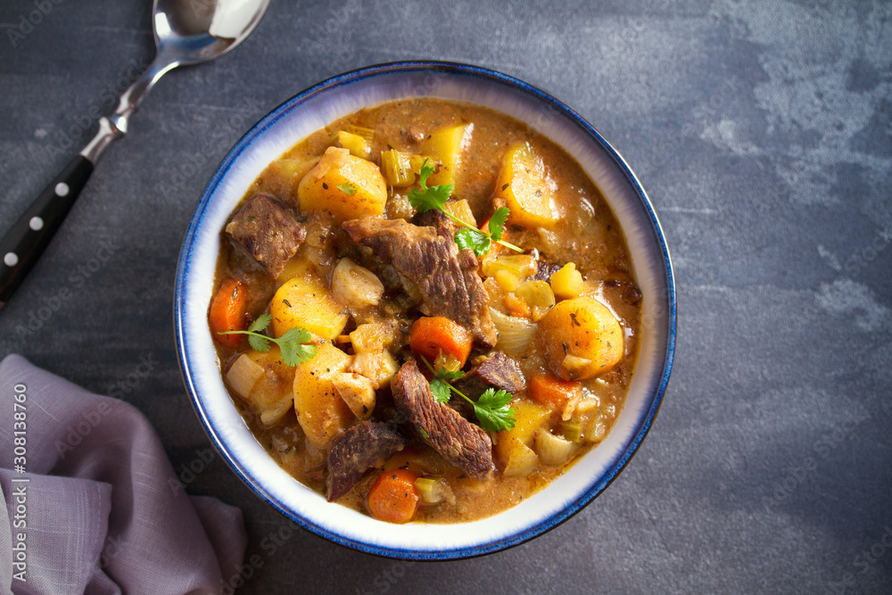 Beef meat stewed with potatoes, carrots and spices in bowl on dark gray background. Overhead horizontal image Beef meat stewed with potatoes, carrots and spices in bowl on dark gray background. Overhead horizontal image