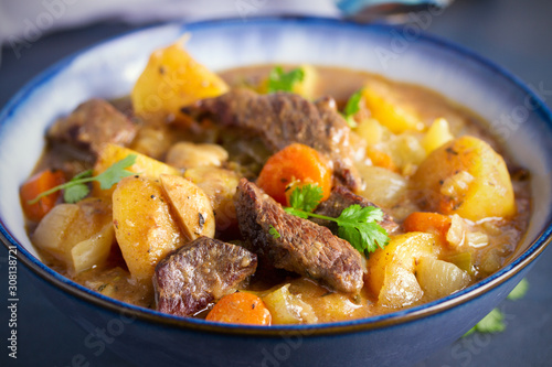 Beef meat stewed with potatoes, carrots and spices in bowl on dark gray background. horizontal image