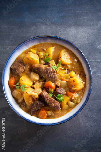 Beef meat stewed with potatoes, carrots and spices in bowl on dark gray background. Overhead vertical image