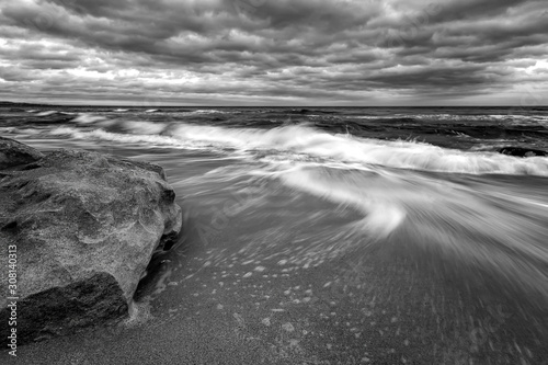 Stunning black and white long exposure seascape with big rock and motion blur waves.