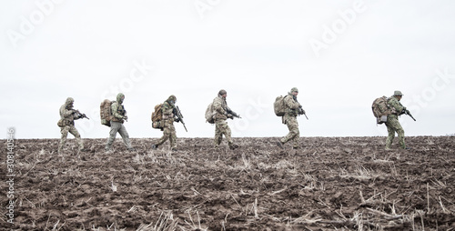 Army soldiers group on march in muddy field