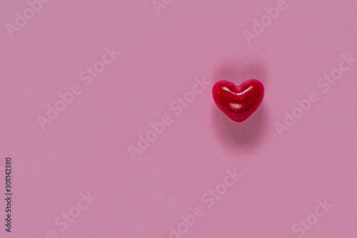 Close-up of a red heart on a pink pastel background, selective focus