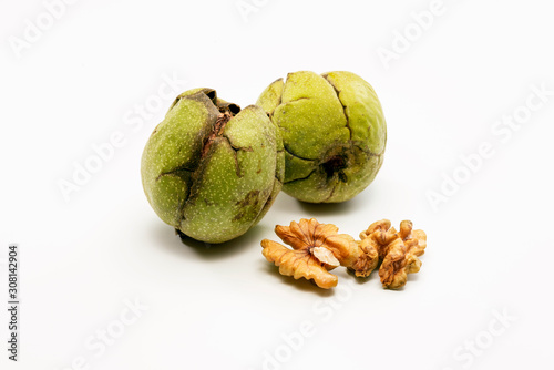 Close up shot of two raw wallnuts with green shell and two pieces of walnut near to them. photo