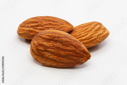 Close up shot of three roasted almonds on a white background.