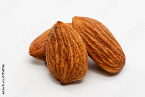 Close up shot of three roasted almonds on a white background.