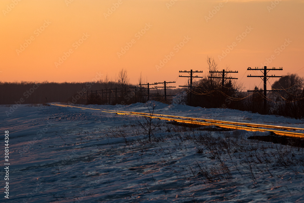 Railway Tracks with Snow under Orange Sunset Sky