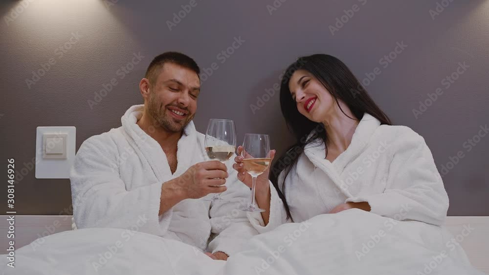 Hotel and travel concept. Young couple in love in bed clink glasses with champagne. Romantic evening in the hotel room Hotel and travel concept. Young couple in love in bed clink glasses with champagne. Romantic evening in the hotel room