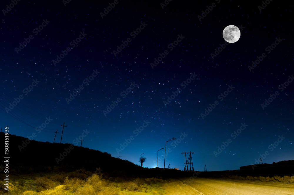 Fototapeta premium Long exposure shot. Mountain Road through the forest on a full moon night. Scenic night landscape of dark blue sky with moon. Azerbaijan