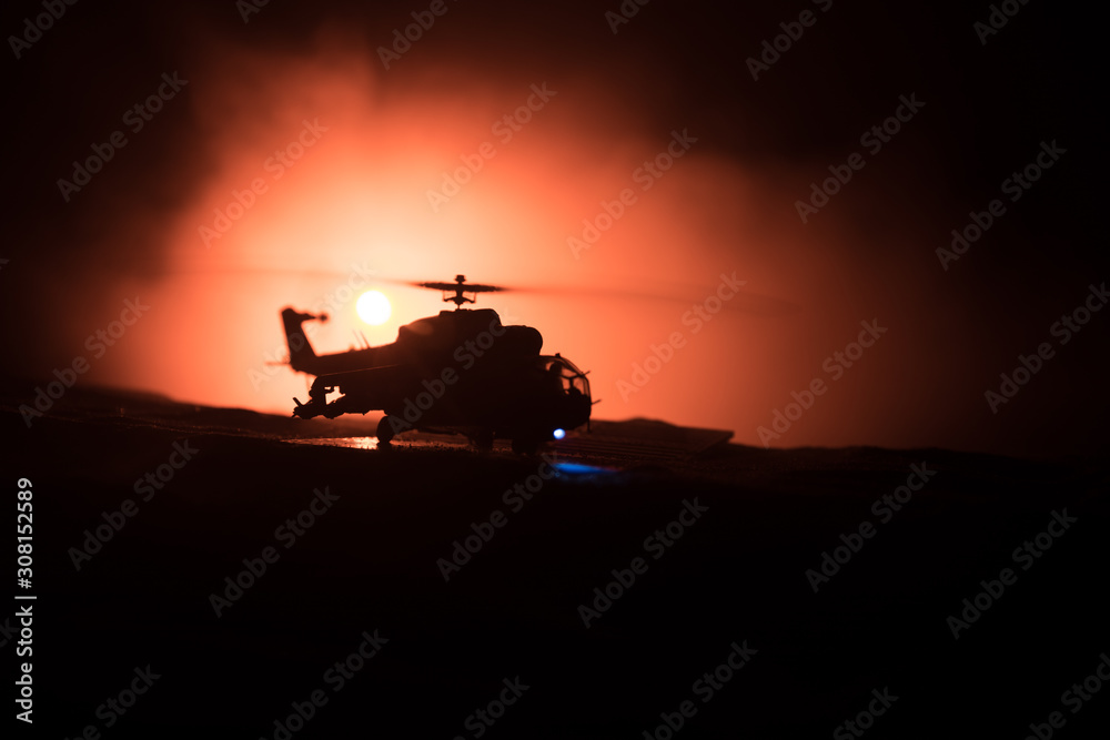 Fototapeta premium Silhouette of military helicopter ready to fly from conflict zone. Decorated night footage with helicopter starting in desert with foggy toned backlit. Selective focus.
