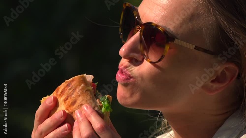 girl eating a delicious sandwich in a park in the sun in summer