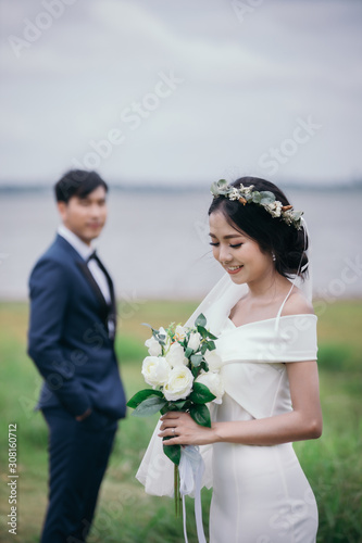 Smiling bride holds a wedding bouquet in her hands and the groom is wearing a suit on background the green meadow.