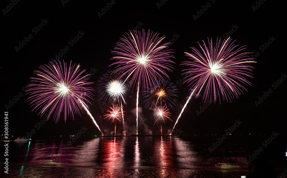 Colorful multiple firework ball (and its reflection) over crowd people on a beach, Pattaya, Thailand